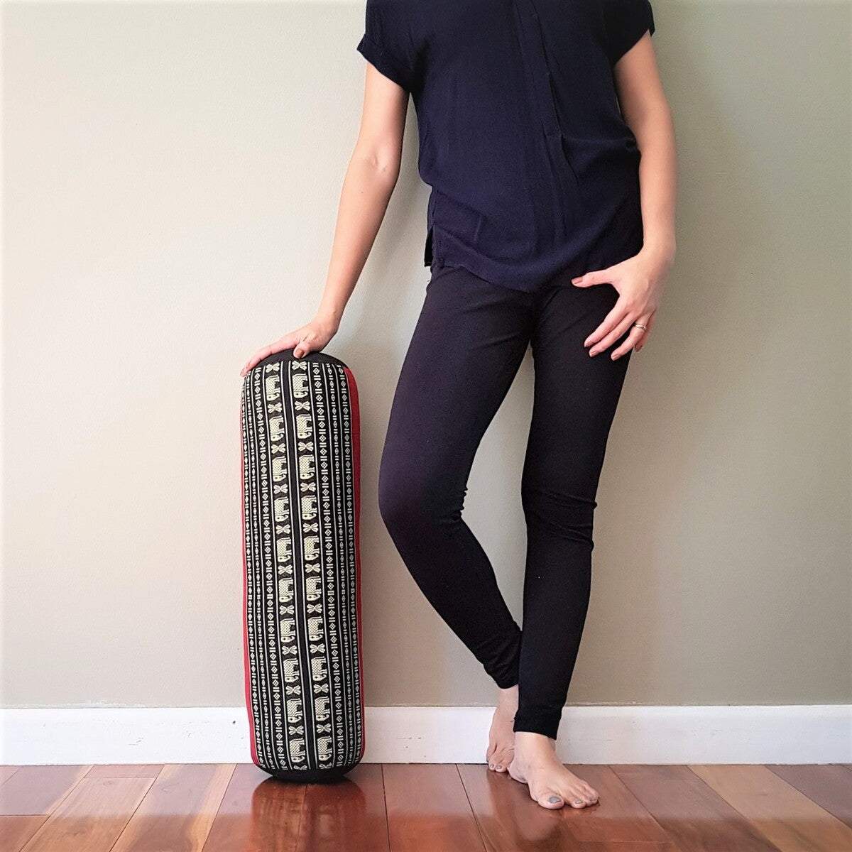 Handmade red yoga bolster with organic kapok filling and elephant pattern, used as a supportive prop for yoga practice.