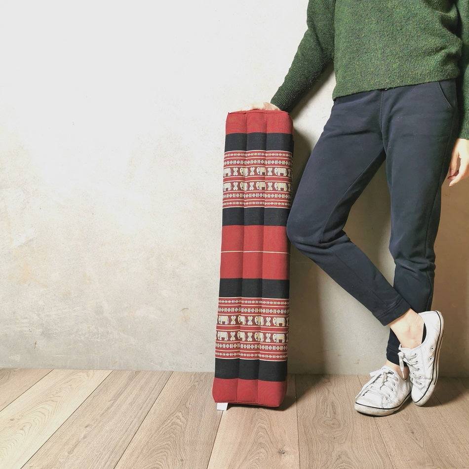 80cm long red and black traditional Thai cotton bolster pillow filled with natural kapok fiber standing beside a person wearing green sweater and navy pants