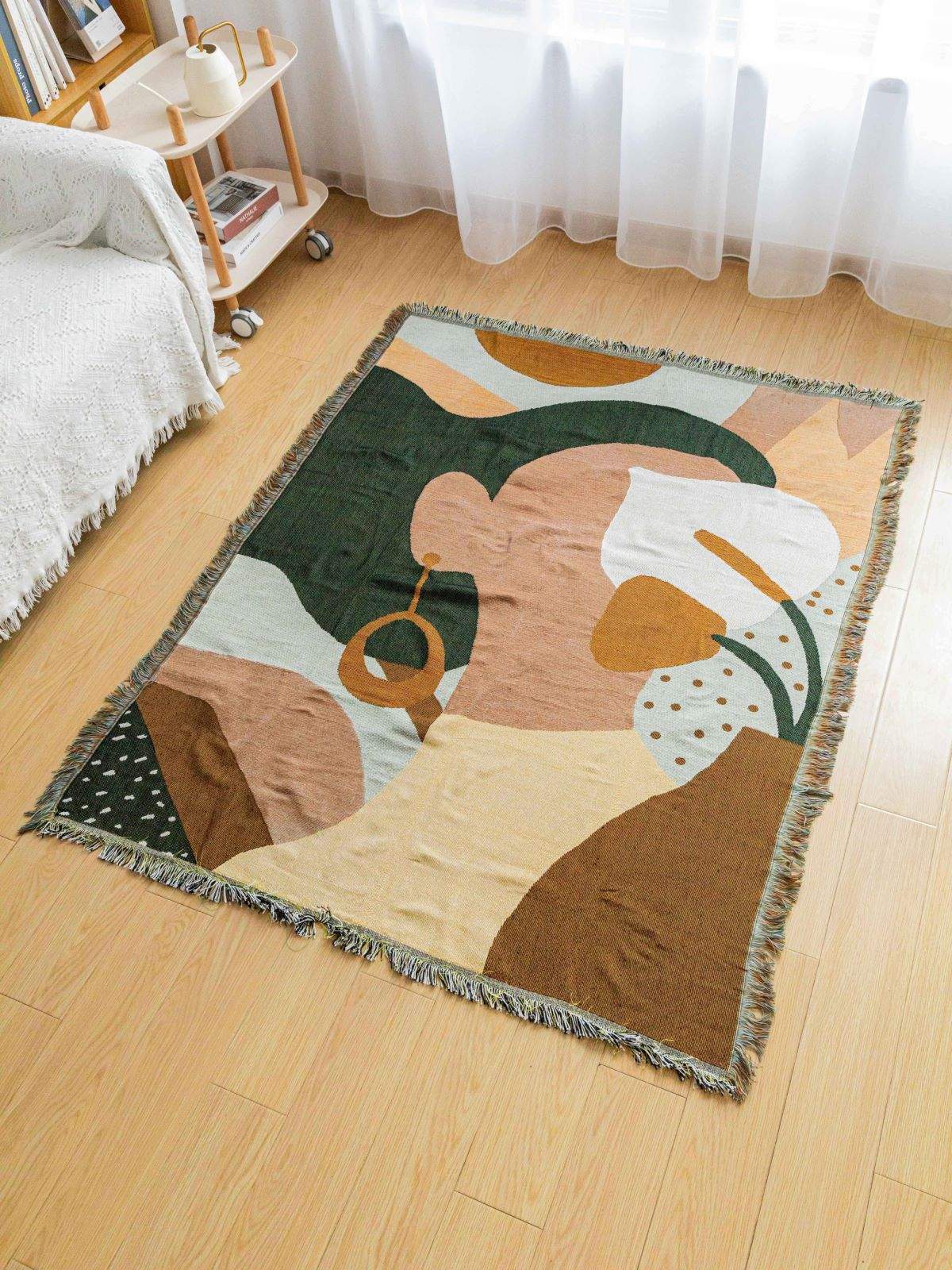 Boho abstract woven blanket with geometric face print and tassel edges in earthy tones on wooden floor
