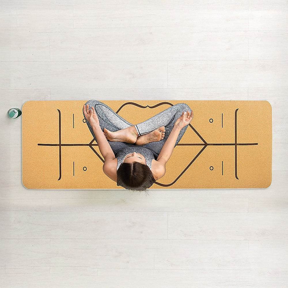 Top-down view of a person practicing yoga on a natural cork TPE eco-friendly yoga mat with printed alignment markings on wooden floor