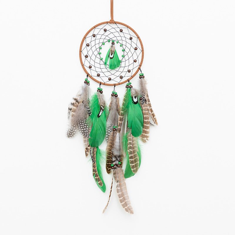 Rounded boho forest dreamcatcher with green and brown feathers and beads hanging on white background