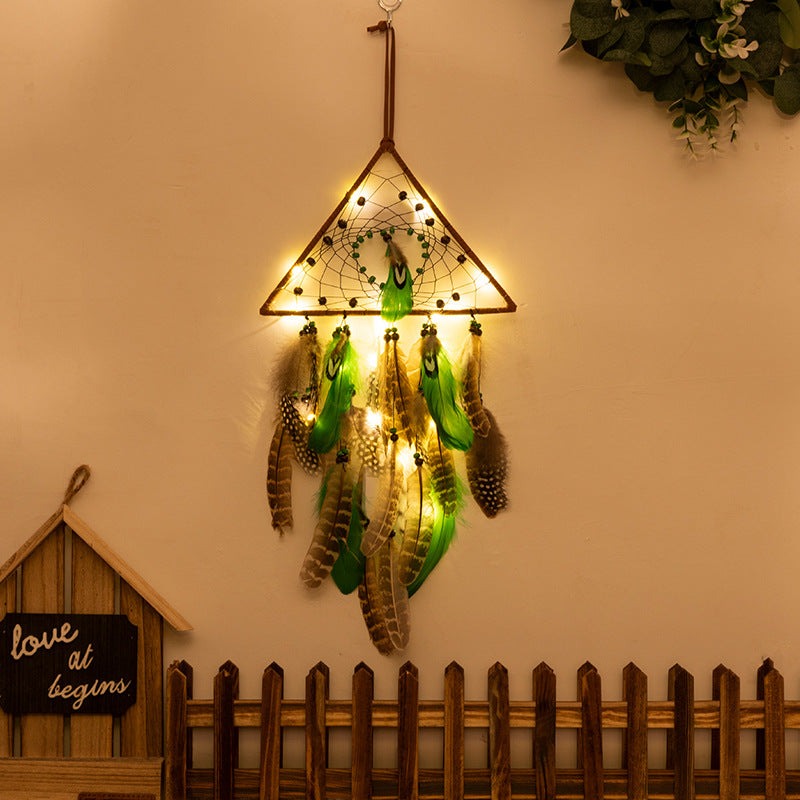Boho forest dreamcatcher wind chime pendant with triangle frame, green feathers, and warm string lights hanging on wall