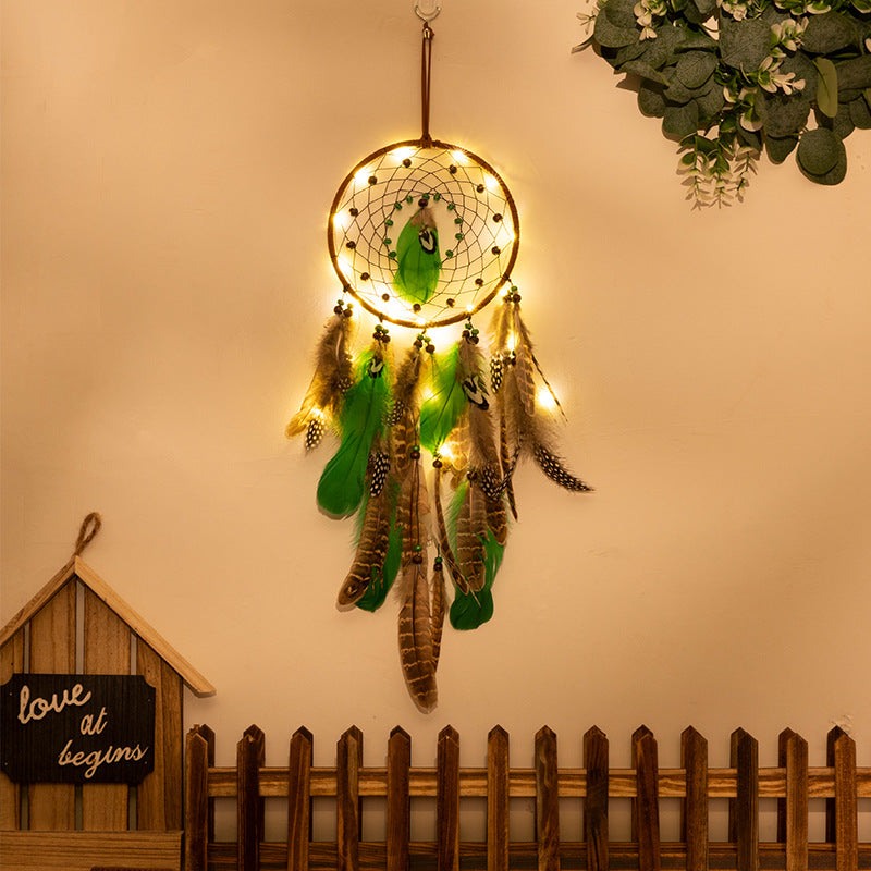 Rounded dreamcatcher wall decor with illuminated lights, green and natural feathers, wooden beads, and a boho forest style design