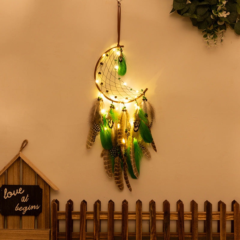 Boho crescent moon dreamcatcher with green feathers and warm LED lights hanging on wall decor