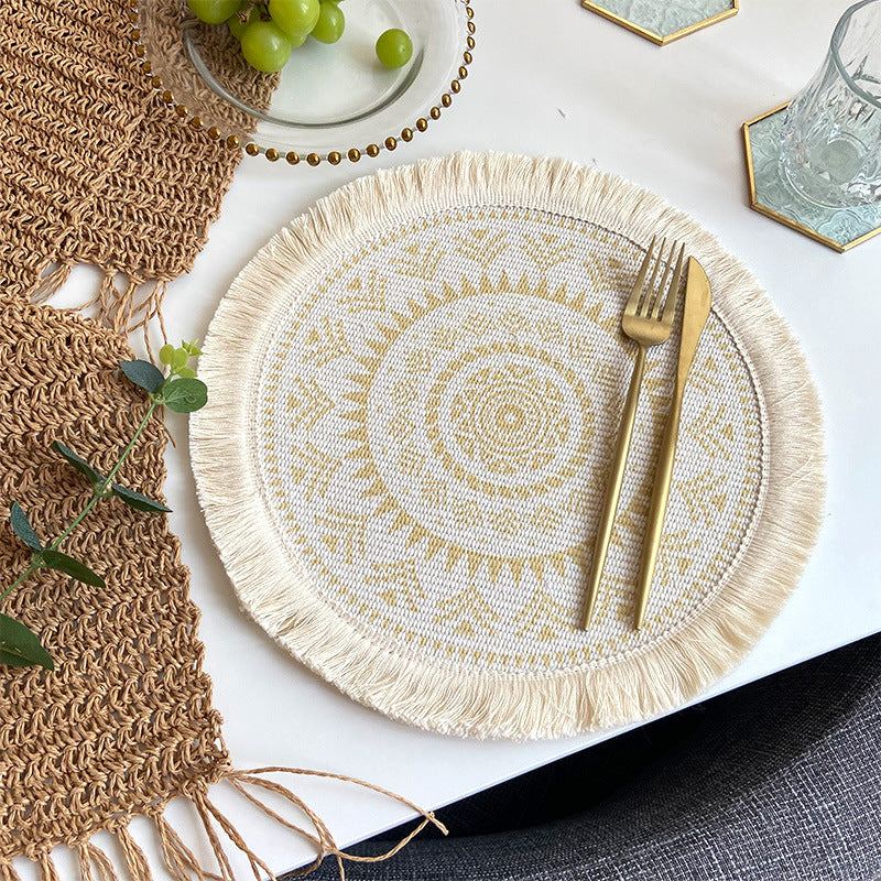 Boho chic woven cotton placemat with beige mandala pattern and fringe tassels on white table with gold cutlery and glassware