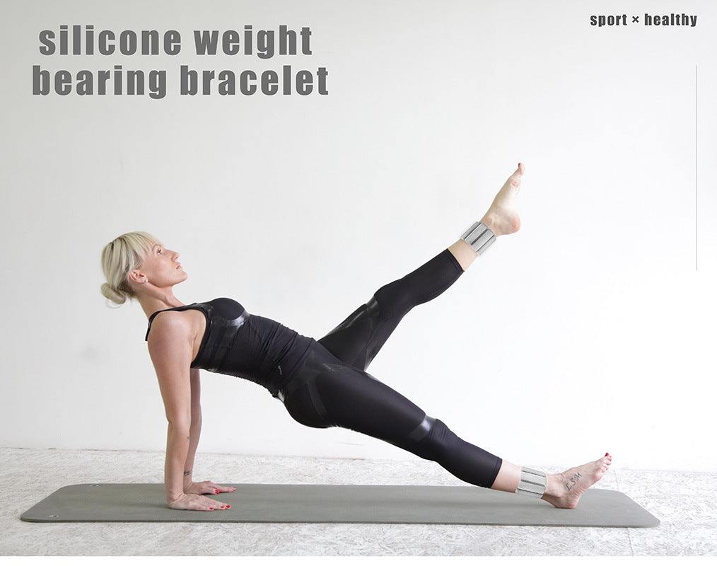 Woman exercising in black workout clothes wearing light orange premium adjustable silicone wrist and ankle weights on a gray mat